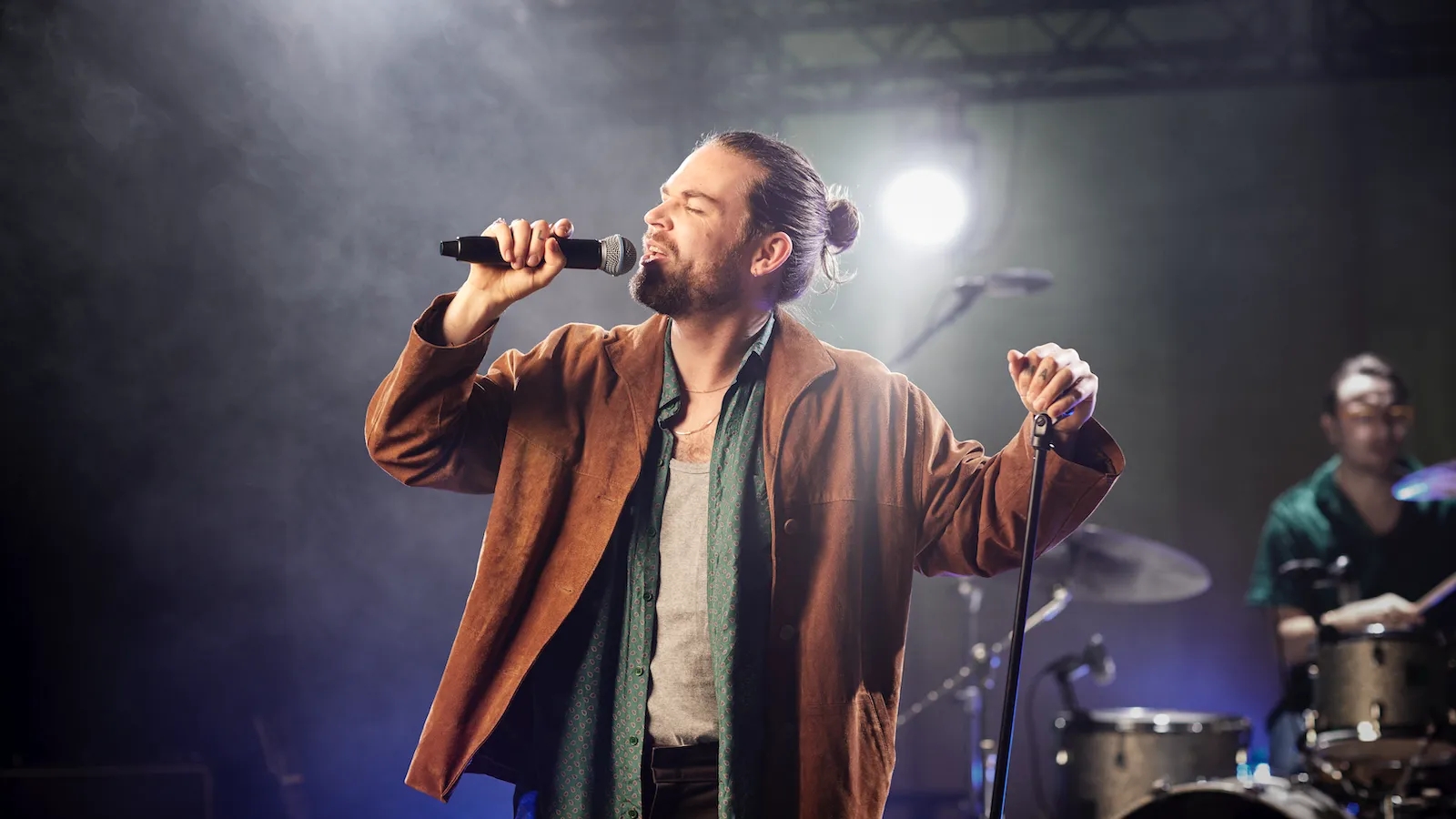 A male singer with a man bun using a wireless SM58 mic